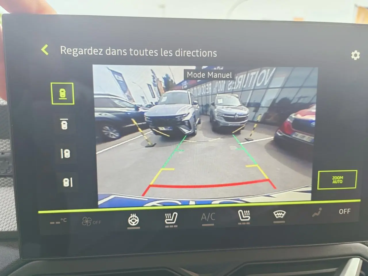 Écran tactile montrant la caméra multivues en mode manuel avec vue arrière sur plusieurs Dacia Duster gris schiste en parking.