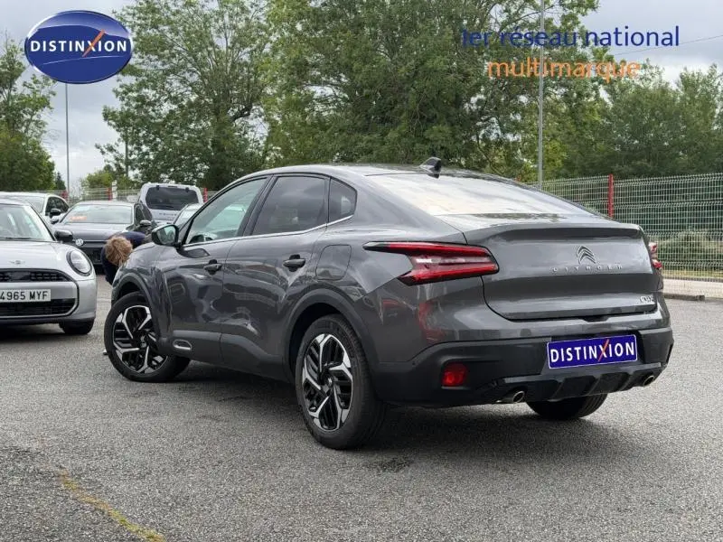 Vue 3/4 arrière droite d'une Citroën C4 X 2024 gris Platinium avec feux arrière LED et jantes noires distinctives.