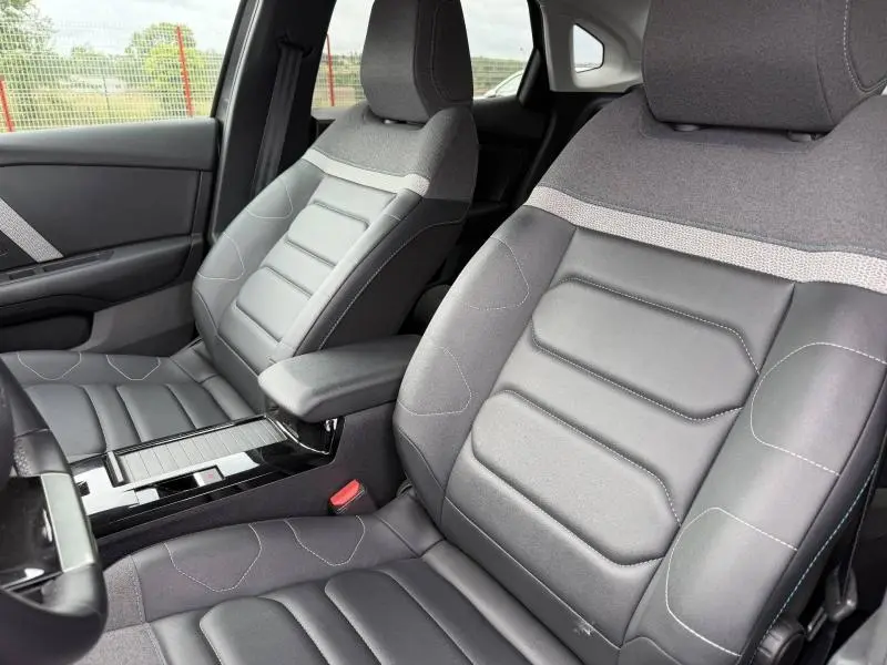 Vue intérieure rapprochée des sièges avant en tissu et cuir gris du Citroën C4 X 2024 avec accoudoir central.