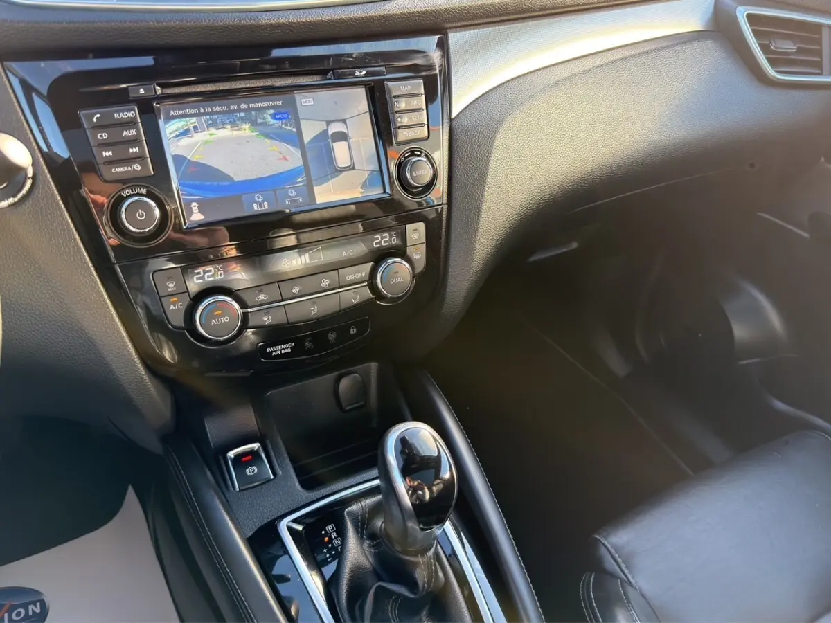 Vue intérieure centrée sur la console centrale du Nissan Qashqai bleu, avec écran tactile et levier de boîte automatique.
