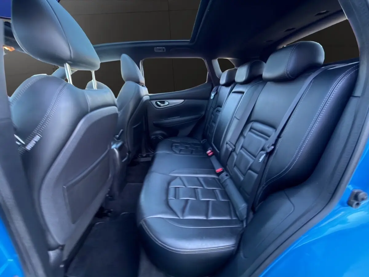 Vue intérieure arrière du Nissan Qashqai bleu 2018, sièges en cuir noir et toit ouvrant panoramique visible.