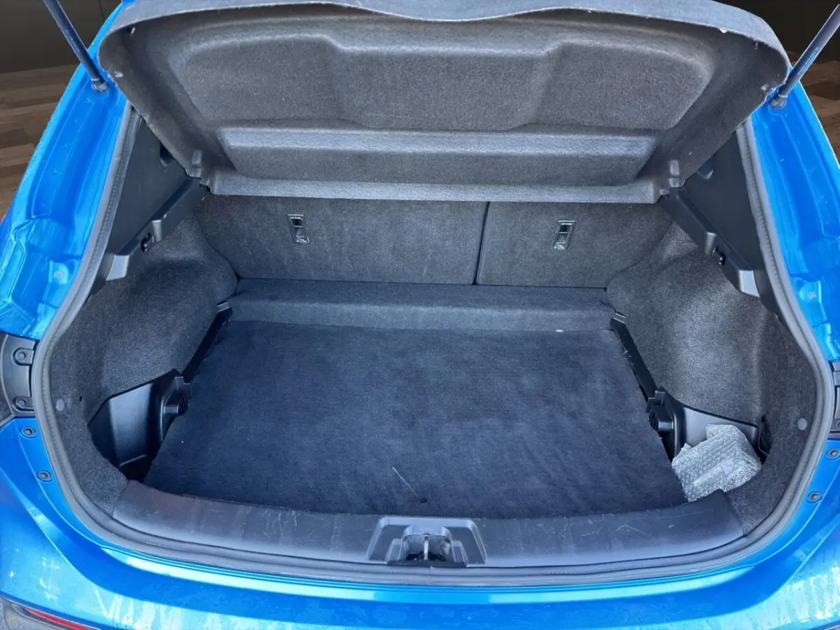 Vue plongeante sur le coffre ouvert d’un Nissan Qashqai bleu, montrant un espace de rangement propre et spacieux.