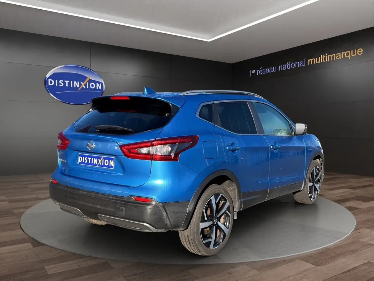 Vue 3/4 arrière droite d'un Nissan Qashqai bleu métallisé avec jantes alliage et toit avec rails chromés.