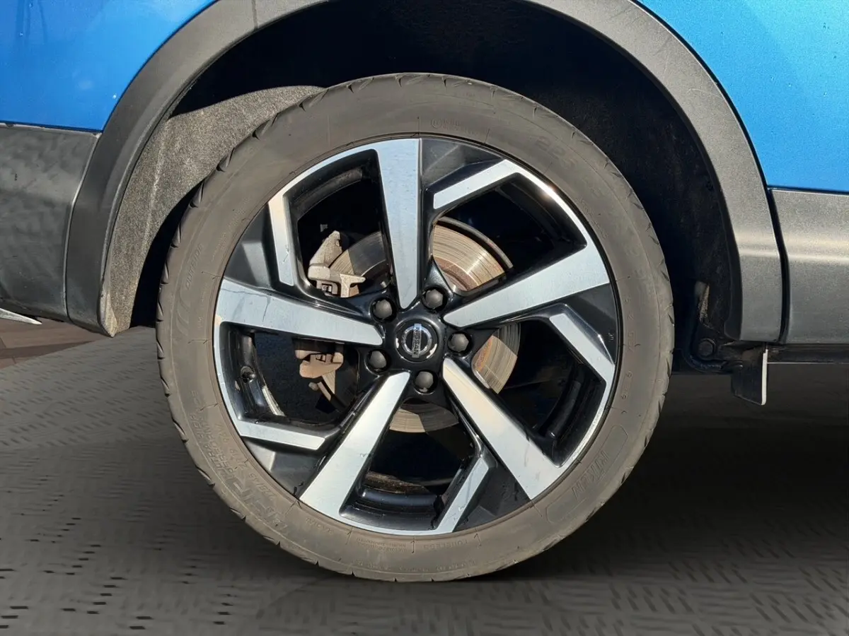 Gros plan sur la roue avant droite du Nissan Qashqai bleu, jante alliage à design moderne bicolore.