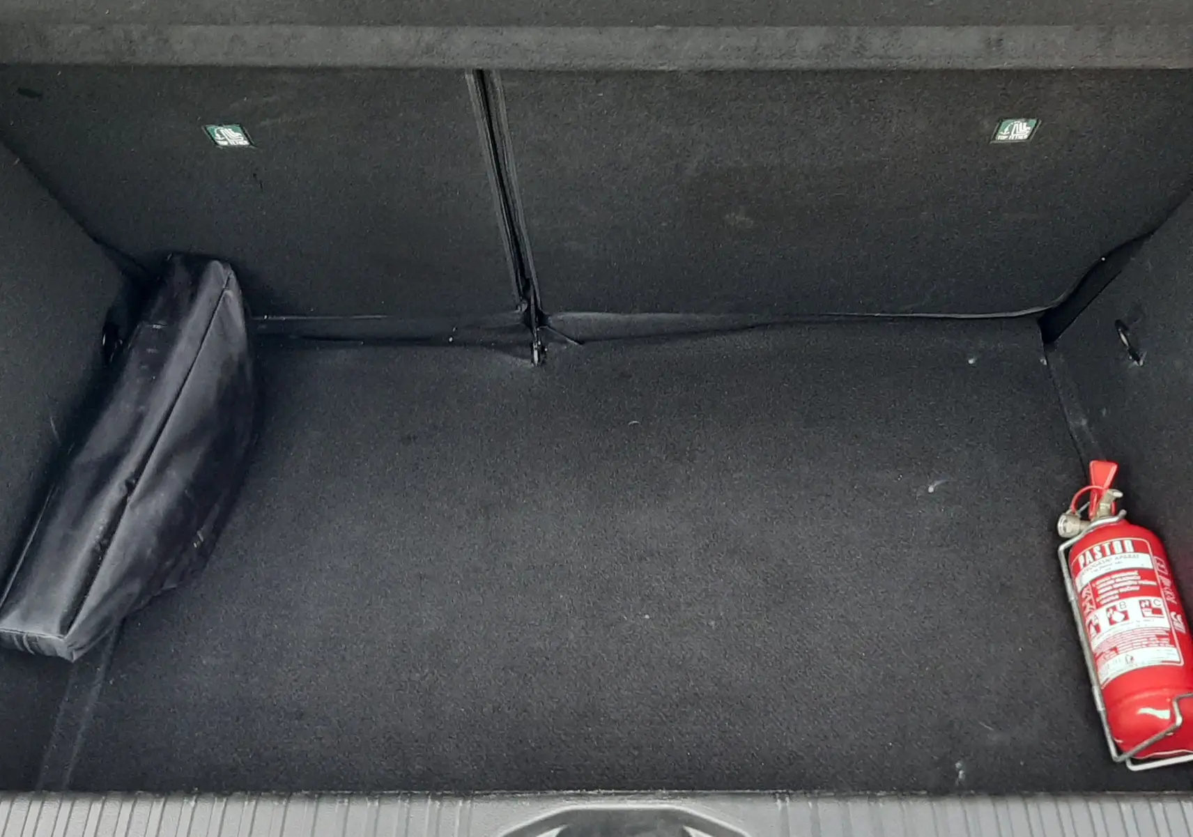 Coffre ouvert d'une Renault Clio V gris schiste, montrant un extincteur rouge et une trousse noire à l'intérieur.