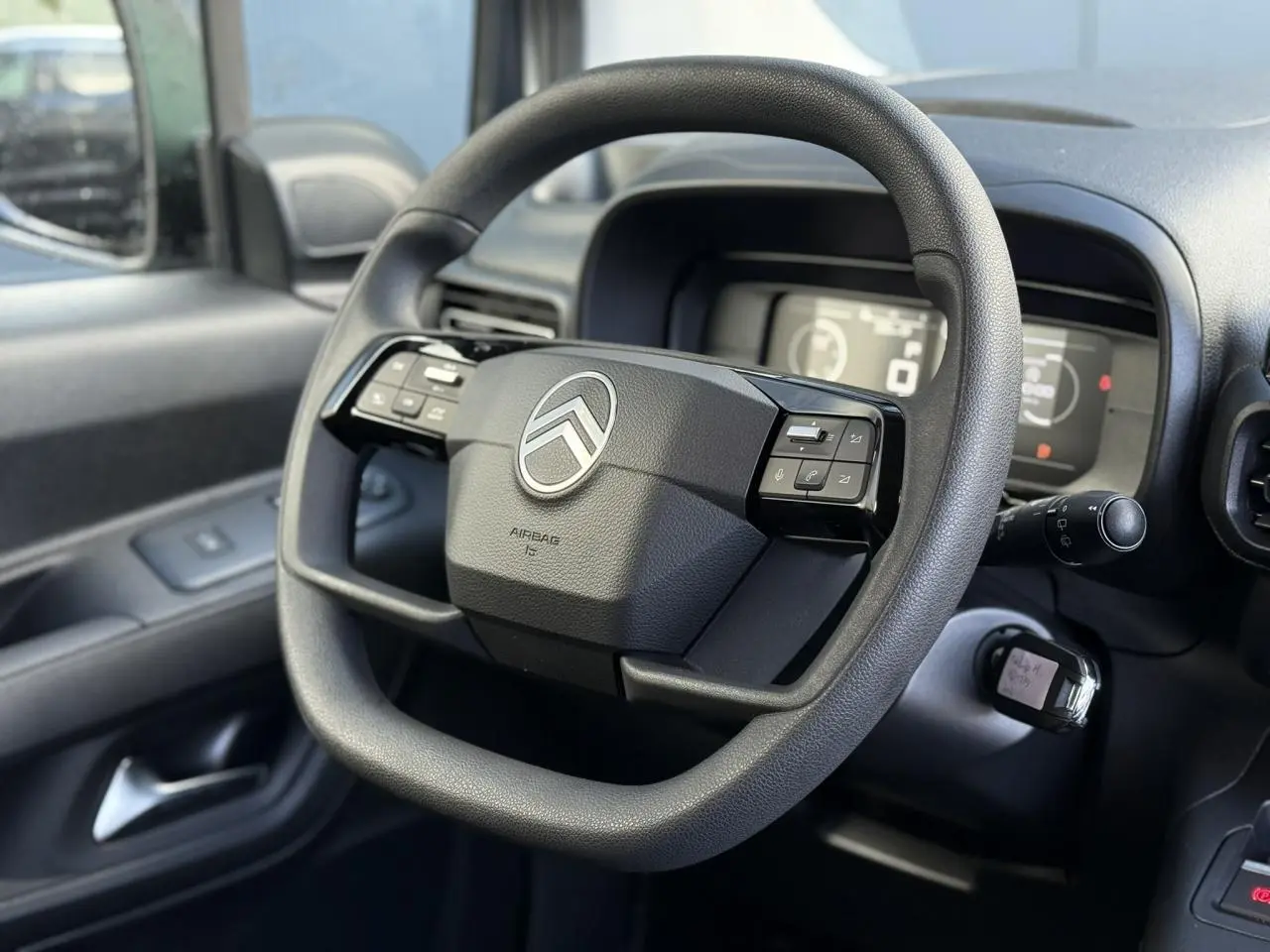 Vue rapprochée du volant multifonctions noir du Citroën Berlingo 2025, côté conducteur avec tableau de bord numérique flou.