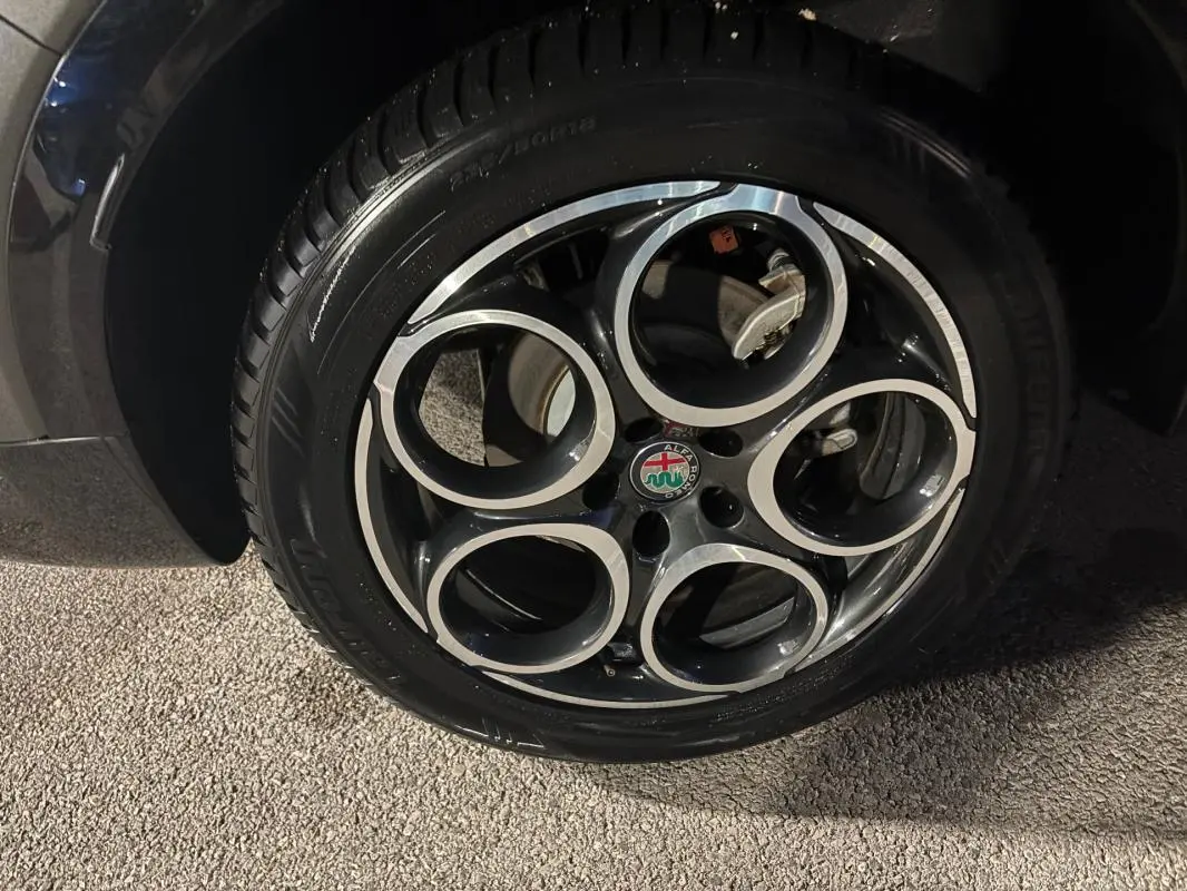 Gros plan sur la jante alliage 18 pouces noire et argentée de l'Alfa Romeo Tonale gris, avec logo central visible.