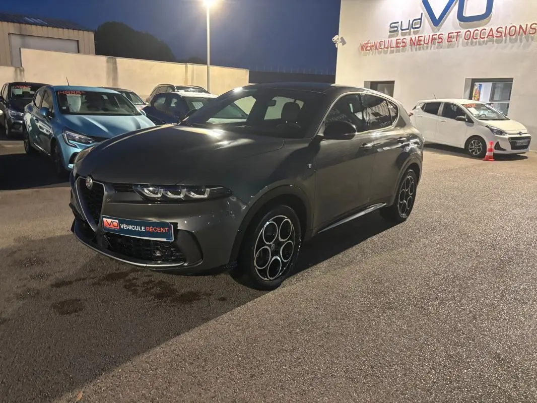 Vue 3/4 avant droit d'une Alfa Romeo Tonale gris métallisé avec jantes alliage 18 pouces, stationnée de nuit.