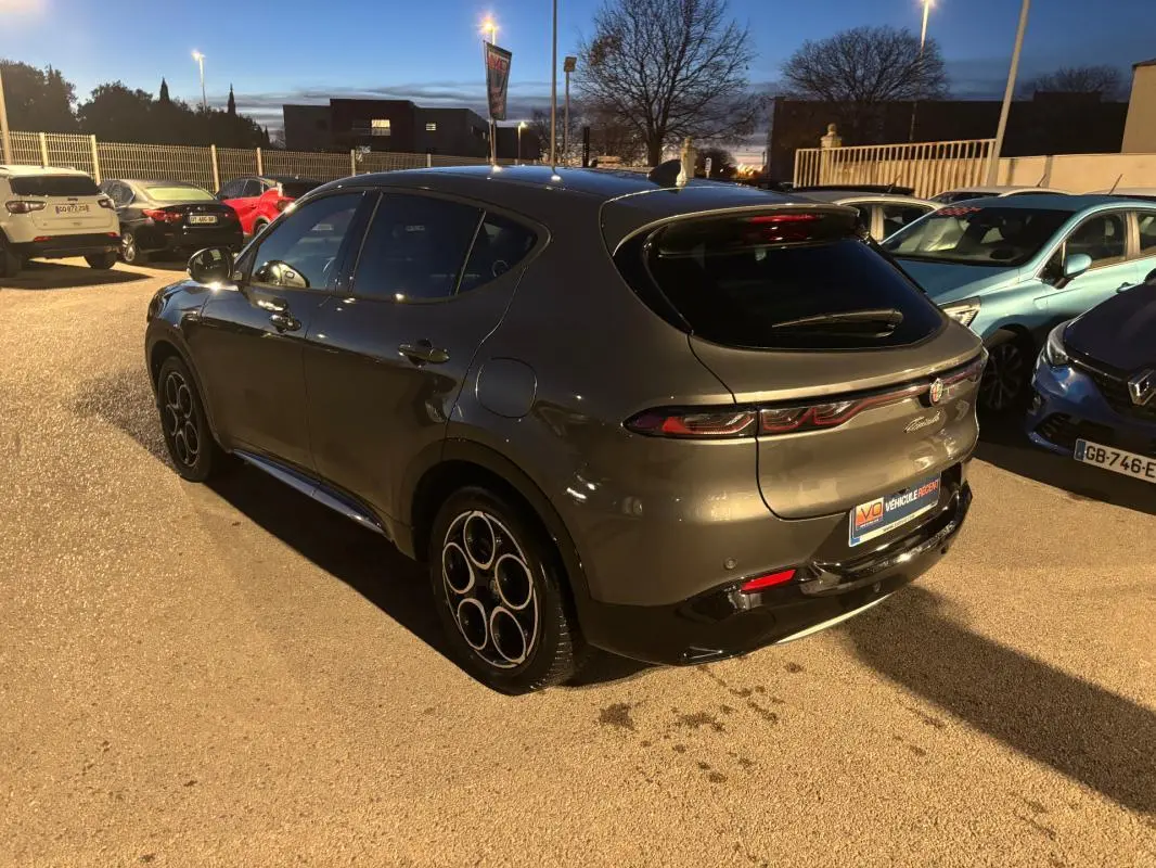 Vue 3/4 arrière droite d'une Alfa Romeo Tonale gris métallisé avec jantes alliage 18 pouces, stationnée en extérieur au crépuscule.