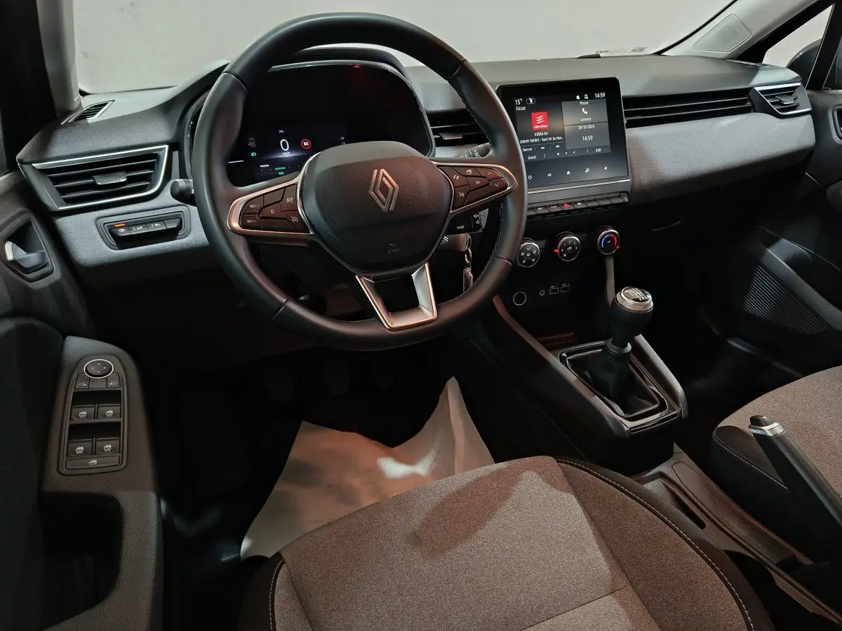 Vue intérieure avant droite de la Renault Clio noire 2025, volant cuir multifonctions et écran tactile central visible.