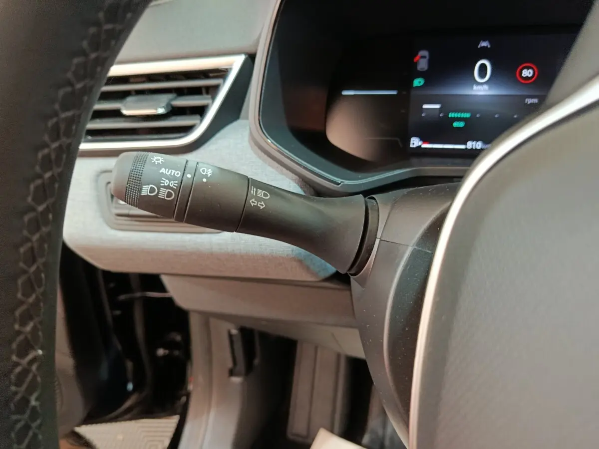 Gros plan sur la commande des phares et clignotants à gauche du volant d’une Renault Clio noire, tableau de bord digital visible.