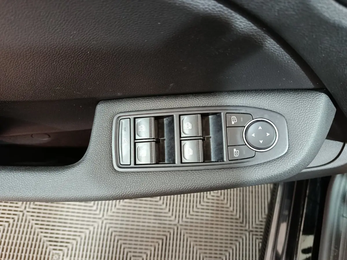 Vue rapprochée des commandes de lève-vitres et rétroviseurs sur la porte côté conducteur d'une Renault Clio noire 2025.