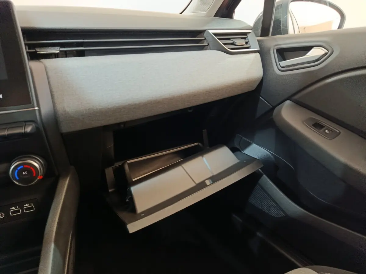 Intérieur de la Renault Clio Evolution Blue dCi 100 2025, vue côté passager sur la boîte à gants ouverte et tableau de bord gris.