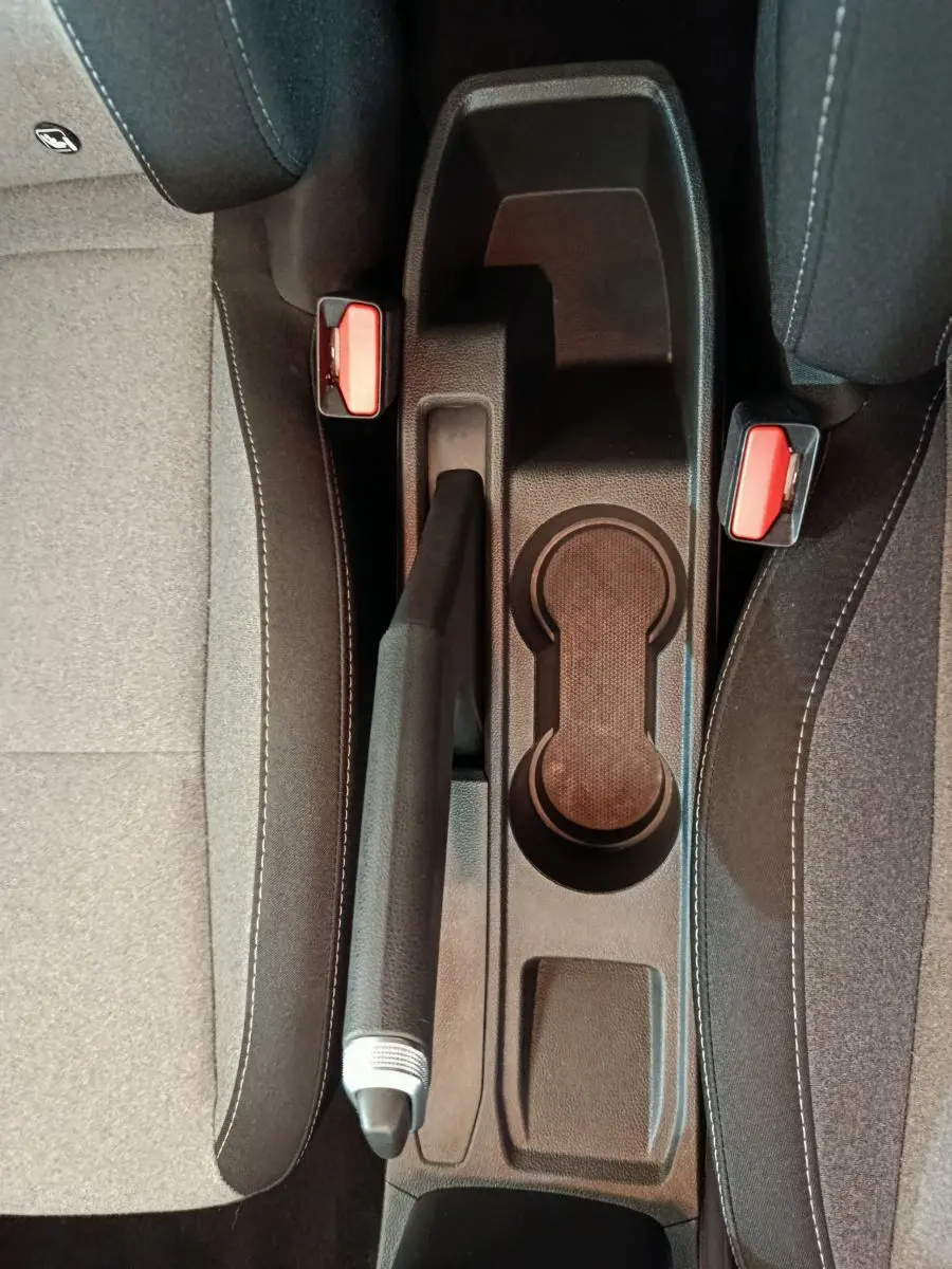 Vue plongeante sur la console centrale noire de la Renault Clio 2025, avec frein à main et porte-gobelets entre sièges gris.