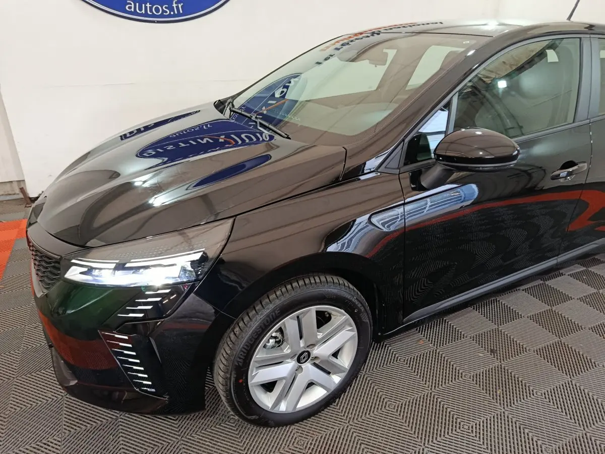 Vue 3/4 avant droit d'une Renault Clio noire 2025 avec feux LED allumés et jantes argentées.