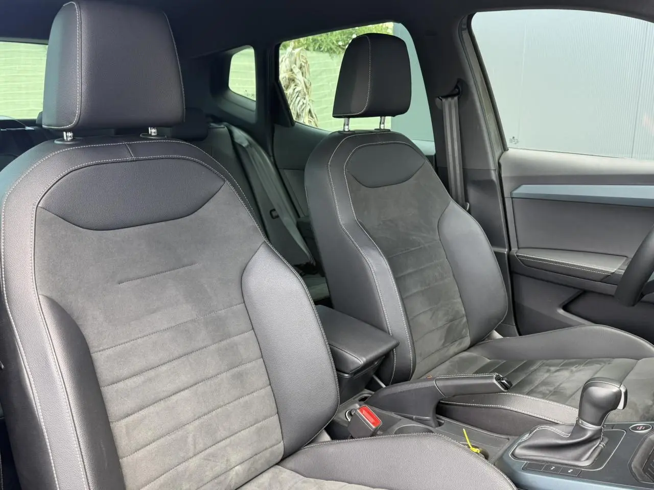 Vue intérieure des sièges avant en cuir-alcantara noir du SEAT Arona TSI 115 DSG Xpérience 2025, avec console centrale et levier de vitesse.