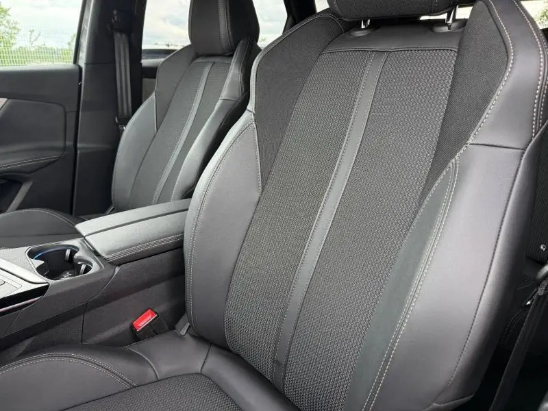 Vue rapprochée des sièges avant en tissu et cuir noir du Peugeot 3008 2024, avec accoudoir central et ceinture rouge visible.
