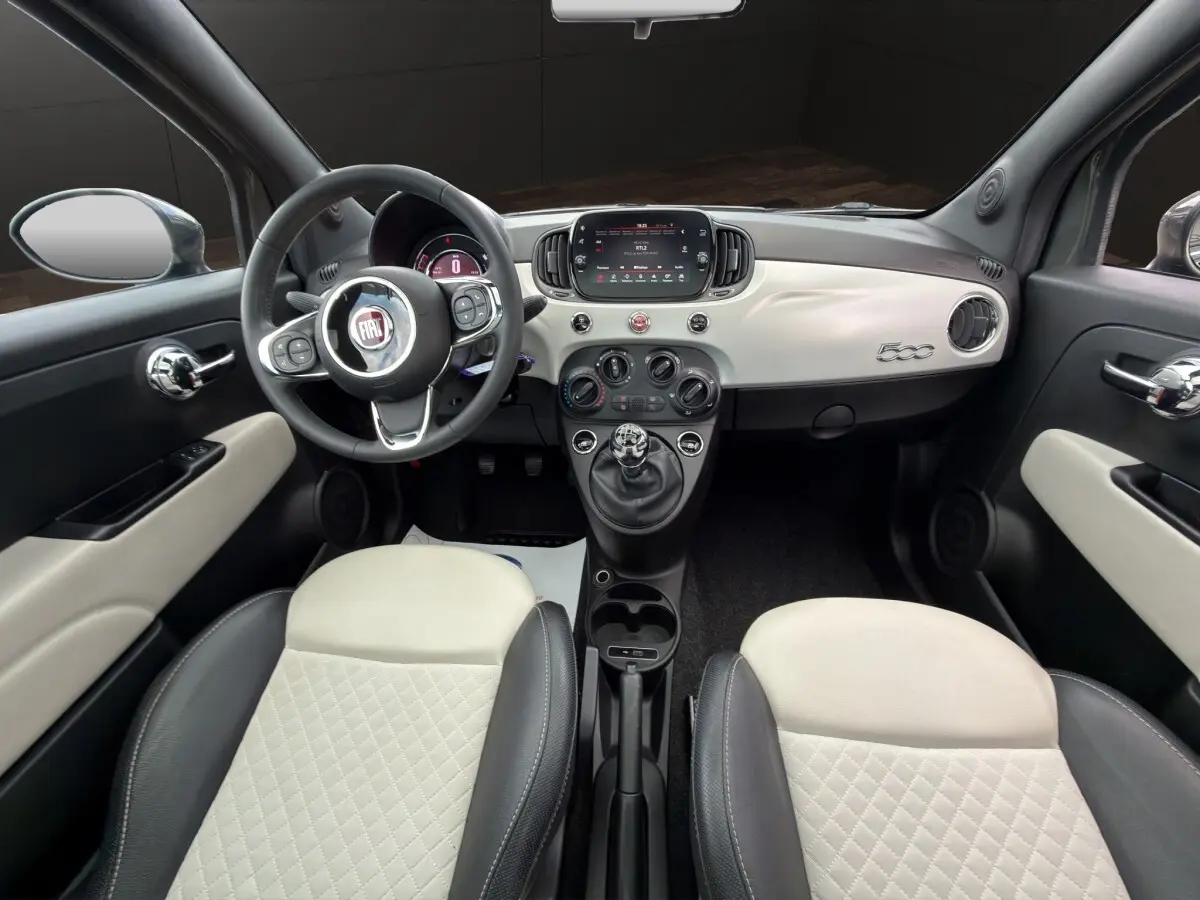 Vue intérieure avant de la Fiat 500 avec tableau de bord blanc, volant cuir multifonctions et sièges bicolores noirs et blancs.