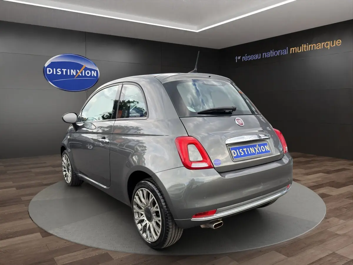 Fiat 500 gris foncé vue 3/4 arrière droit, avec jantes alliage et sortie d’échappement chromée visible.