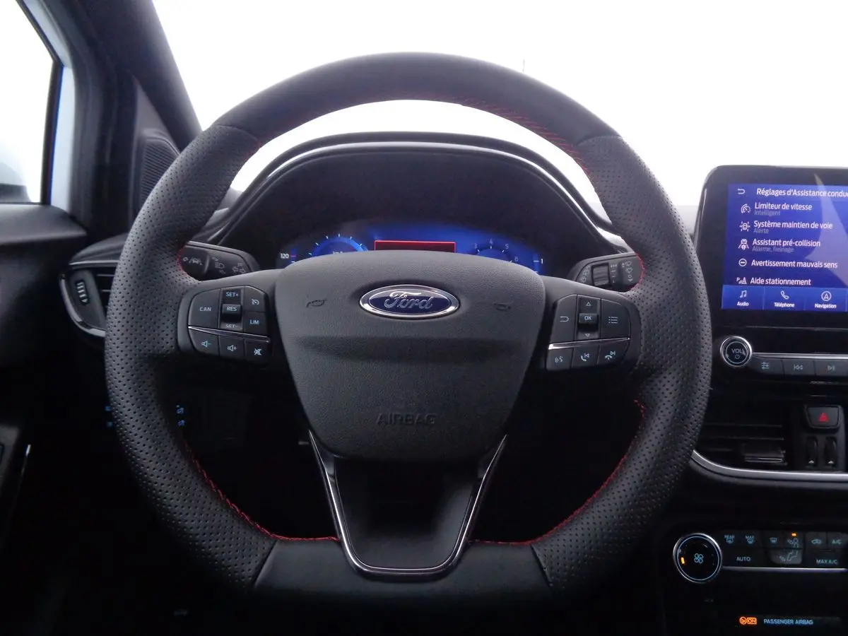 Vue rapprochée du volant perforé avec surpiqûres rouges du Ford Puma blanc, tableau de bord et écran tactile en arrière-plan.