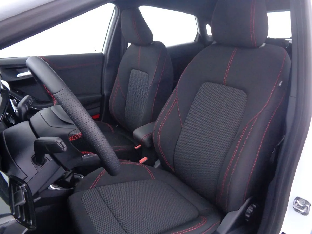 Intérieur avant du Ford Puma blanc 2022, sièges noirs avec surpiqûres rouges et volant en cuir perforé.