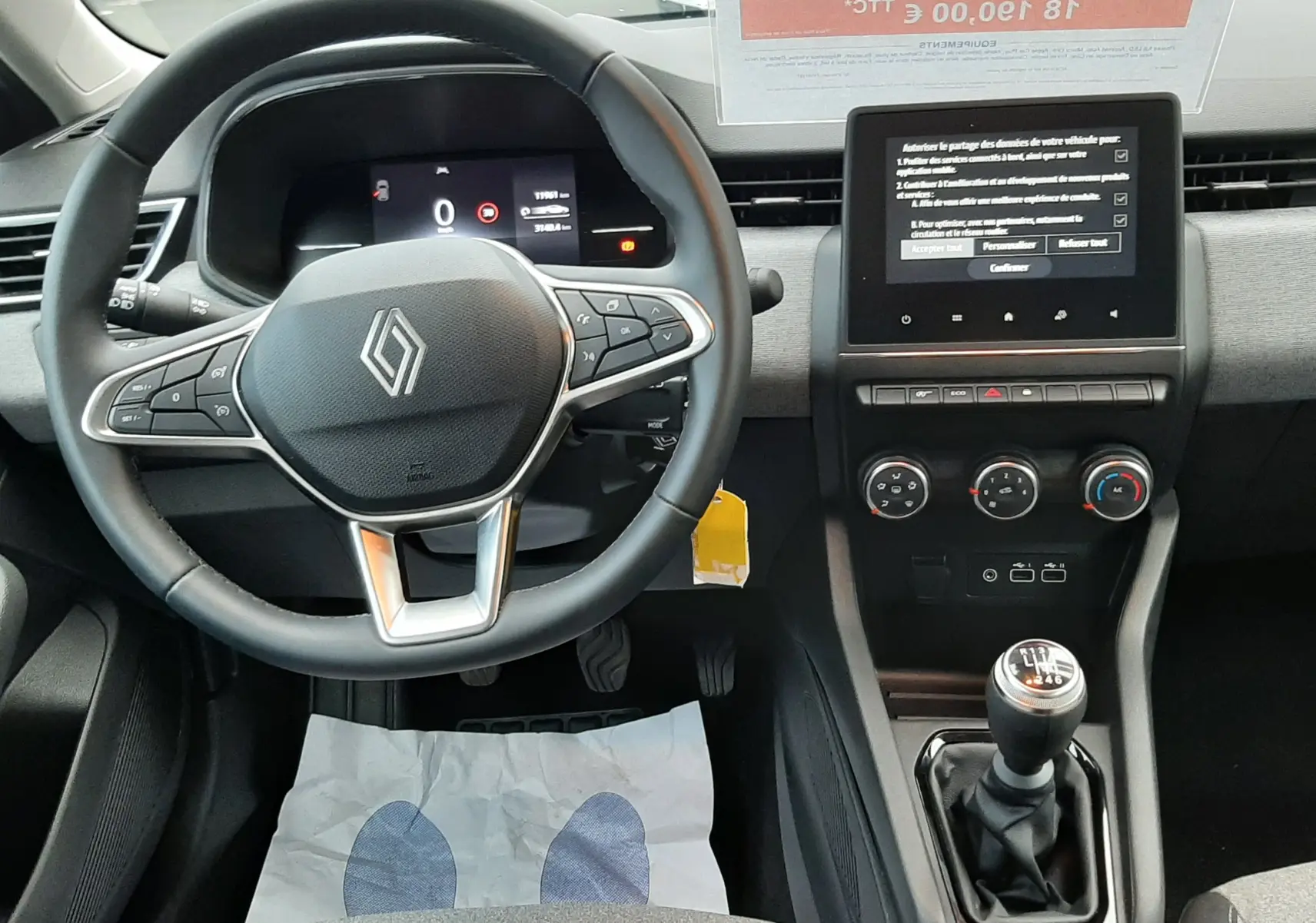 Vue intérieure avant centrée sur le volant Renault et la console centrale avec boîte manuelle dans une Clio V gris schiste 2025.