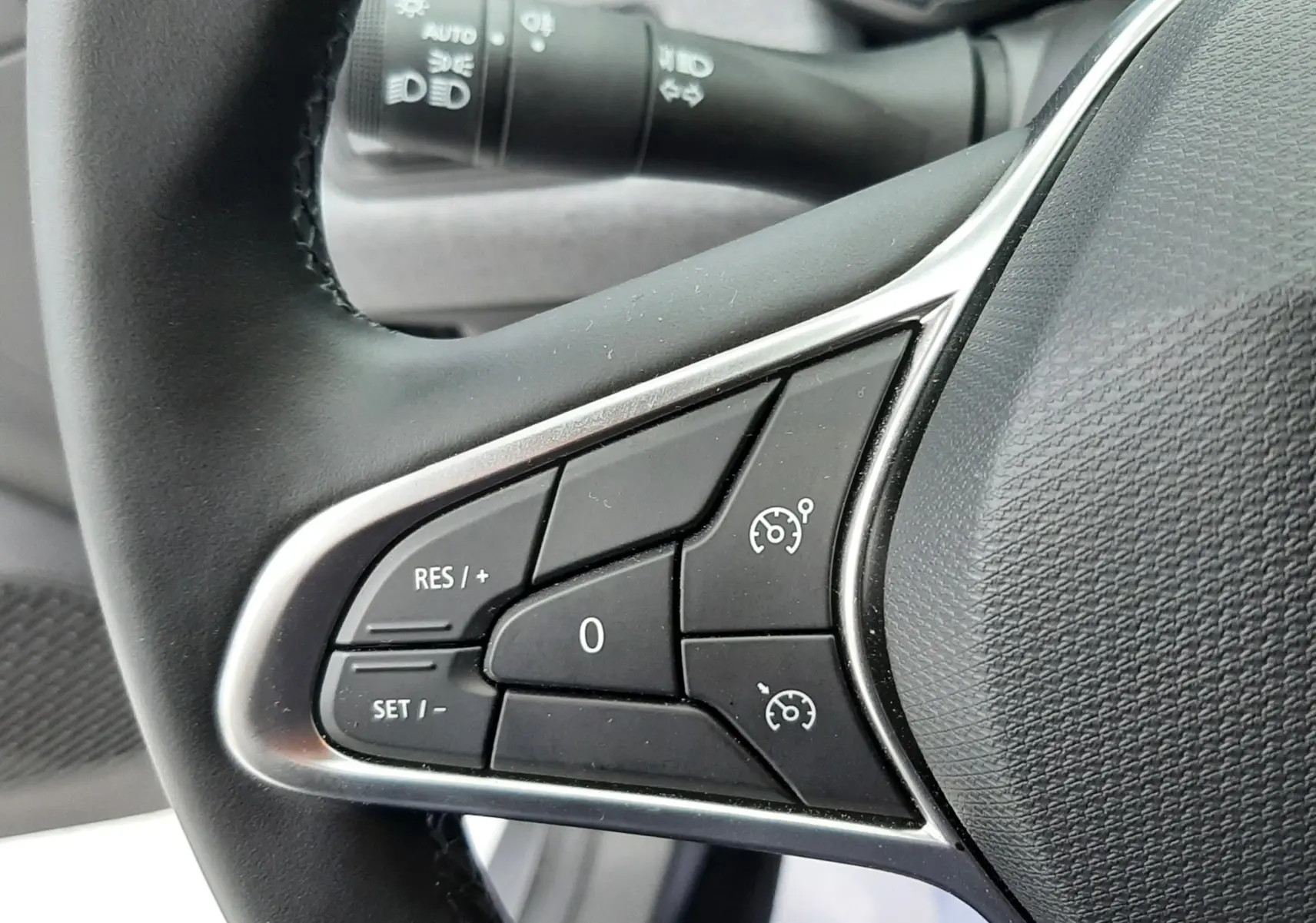 Gros plan sur les commandes de régulateur de vitesse au volant d'une Renault Clio V gris schiste, intérieur tissu gris.