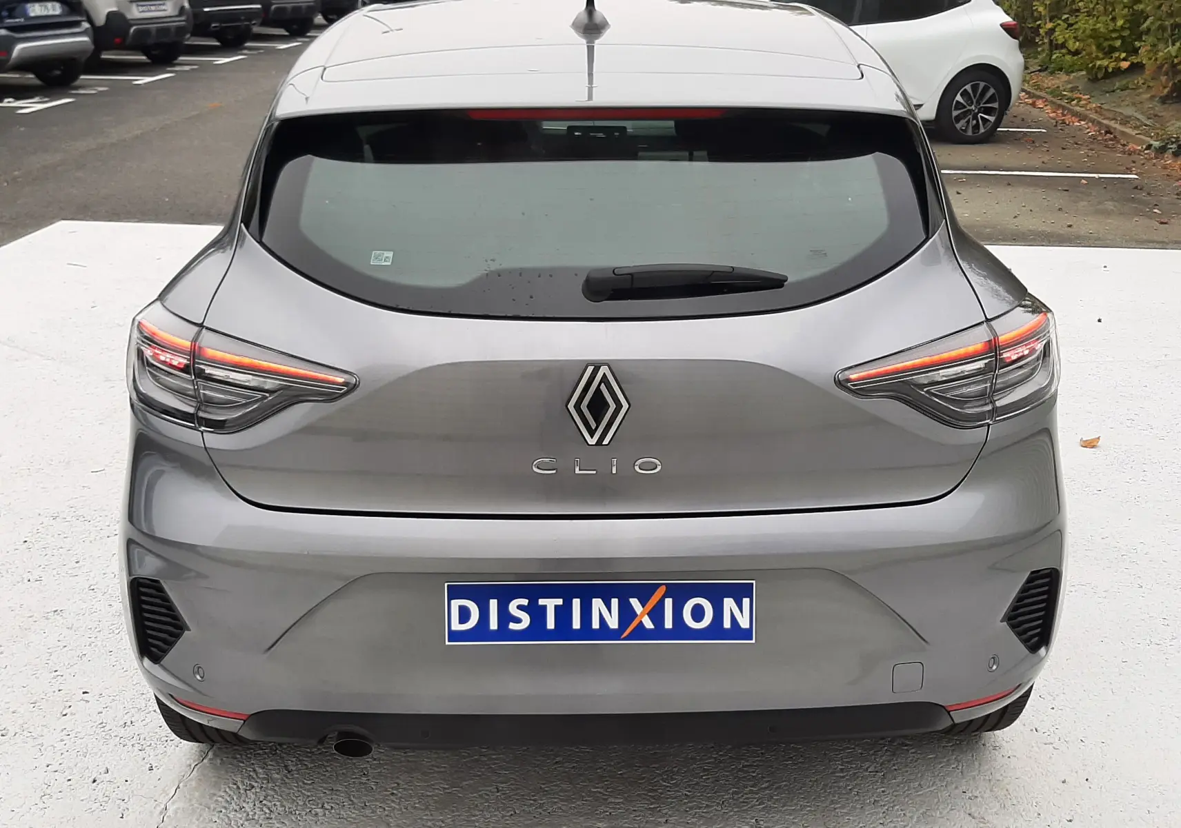 Vue arrière d'une Renault Clio V gris schiste avec feux LED allumés et plaque d'immatriculation Distinxion visible.