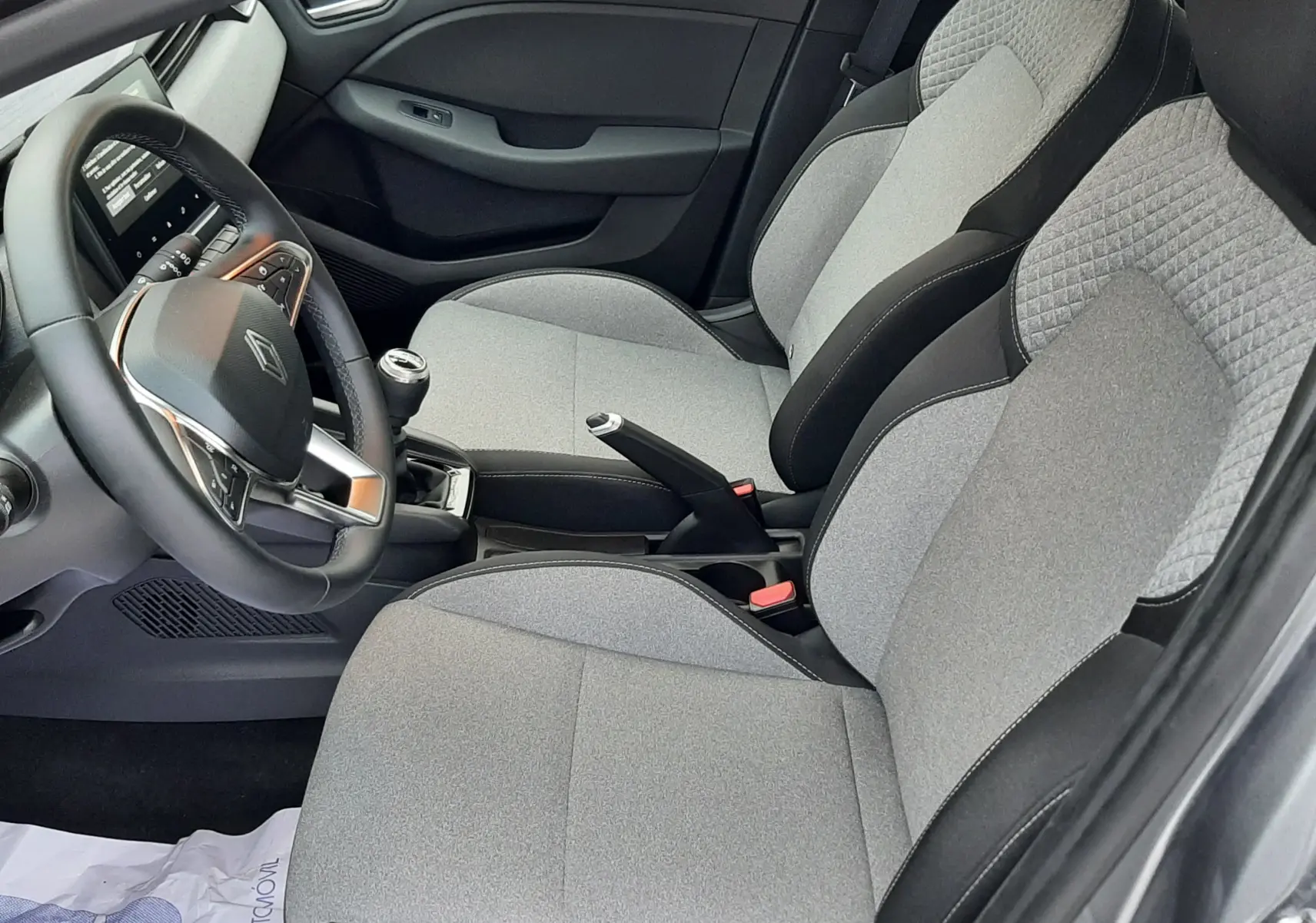 Vue intérieure côté conducteur de la Renault Clio V TCE 90ch Evolution 2025 avec sièges tissu gris et volant multifonction.