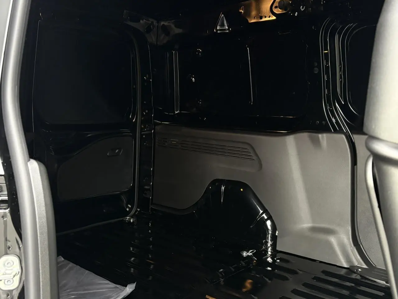 Vue intérieure de la zone de chargement noire du Citroën Berlingo Van XL 2025, avec cloison et porte latérale ouverte.