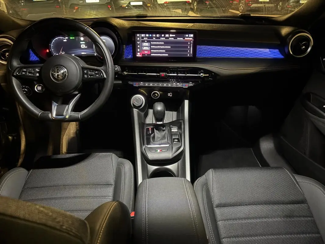 Vue intérieure avant de l'Alfa Romeo Tonale 2023 avec tableau de bord noir et éclairage d'ambiance bleu.