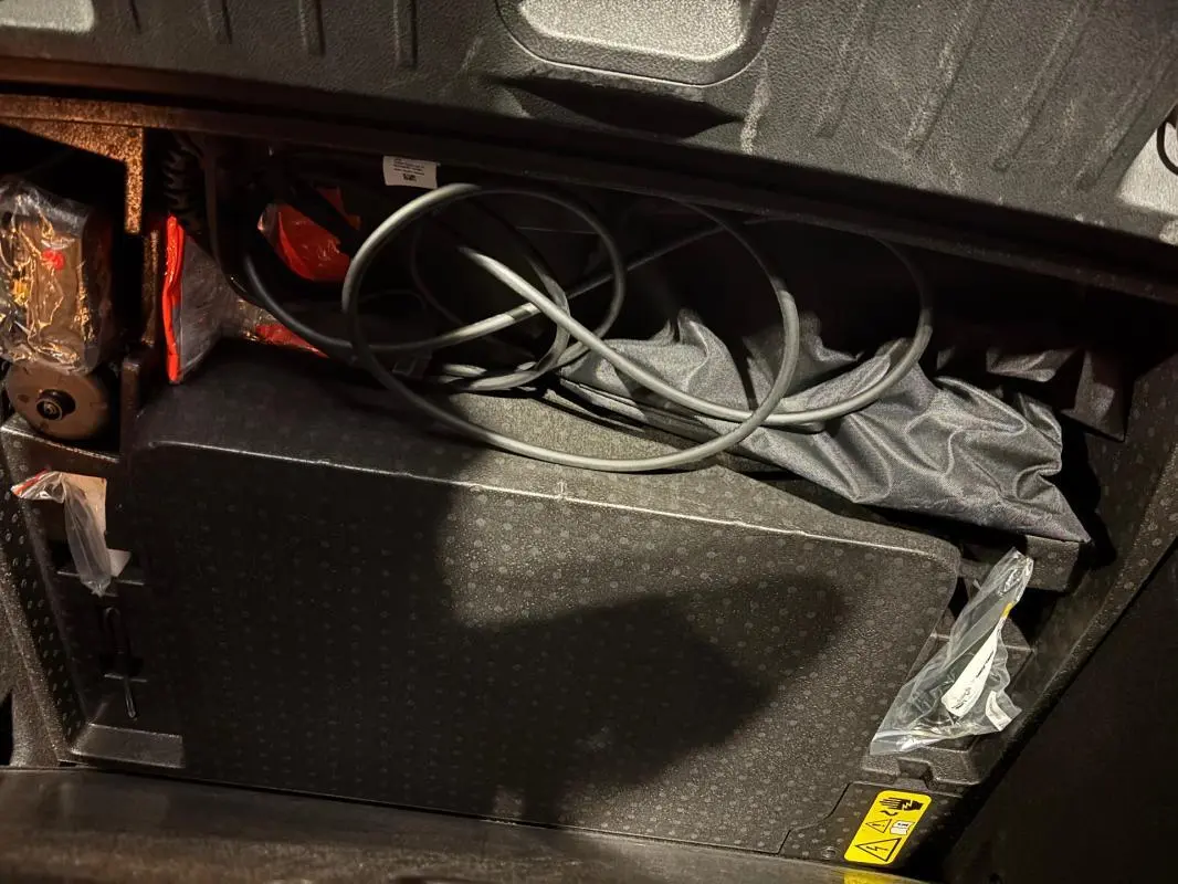 Vue plongeante sur le coffre de l'Alfa Romeo Tonale gris, montrant le rangement avec câbles et accessoires de recharge.