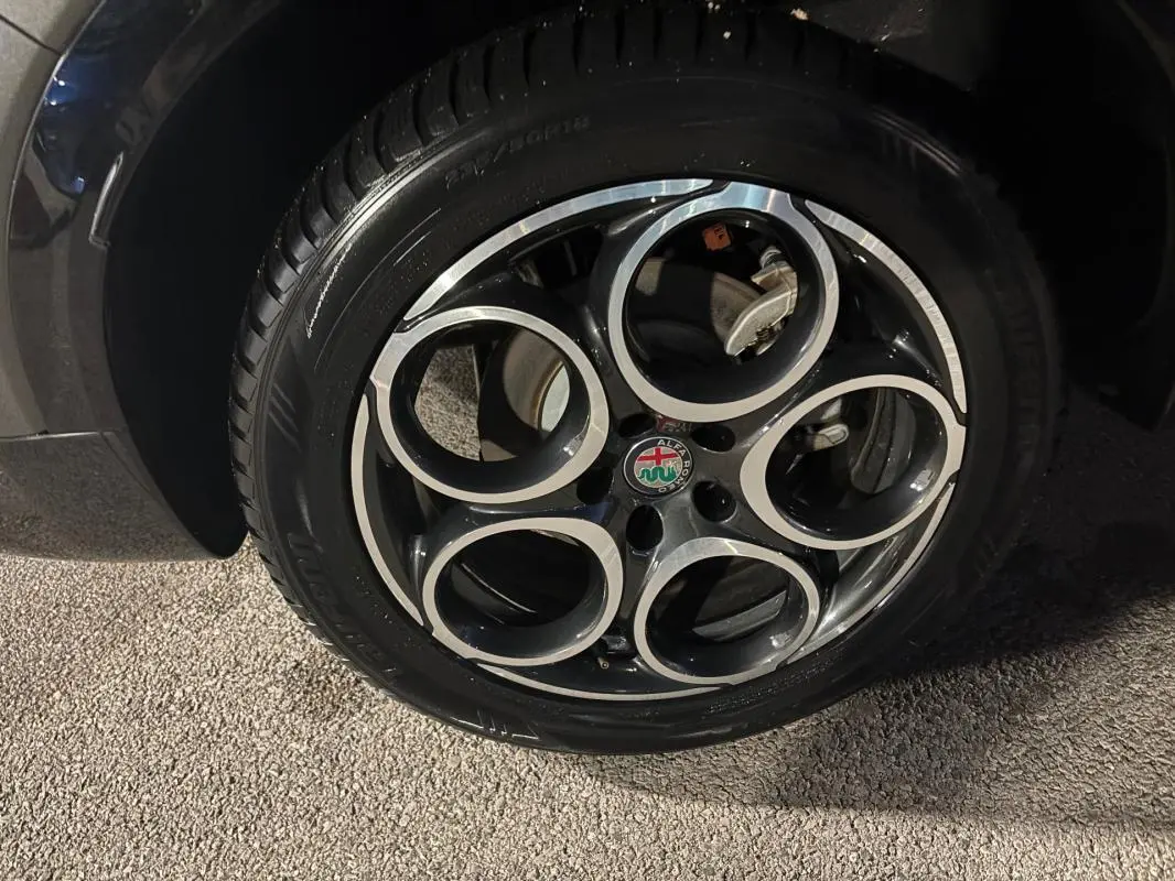 Gros plan sur la jante alliage 18 pouces noire et argentée de l'Alfa Romeo Tonale gris, avec logo central visible.