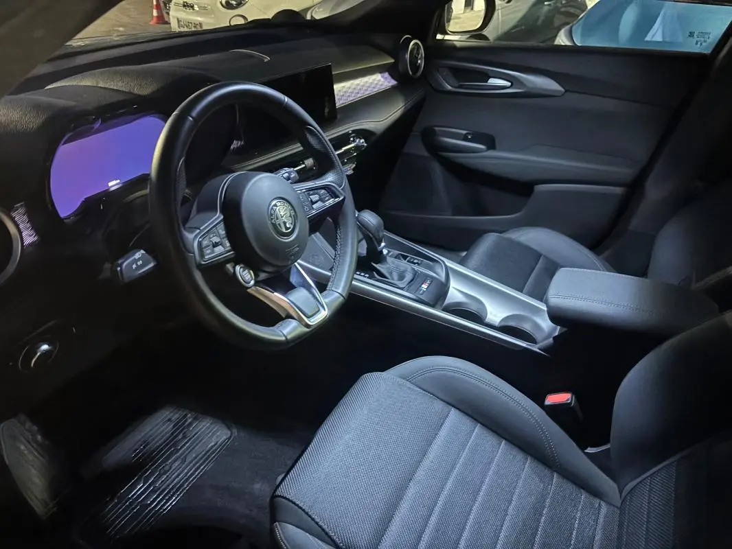 Intérieur de l'Alfa Romeo Tonale 2023 vu côté conducteur, volant sport, console centrale avec boîte auto et accoudoir.