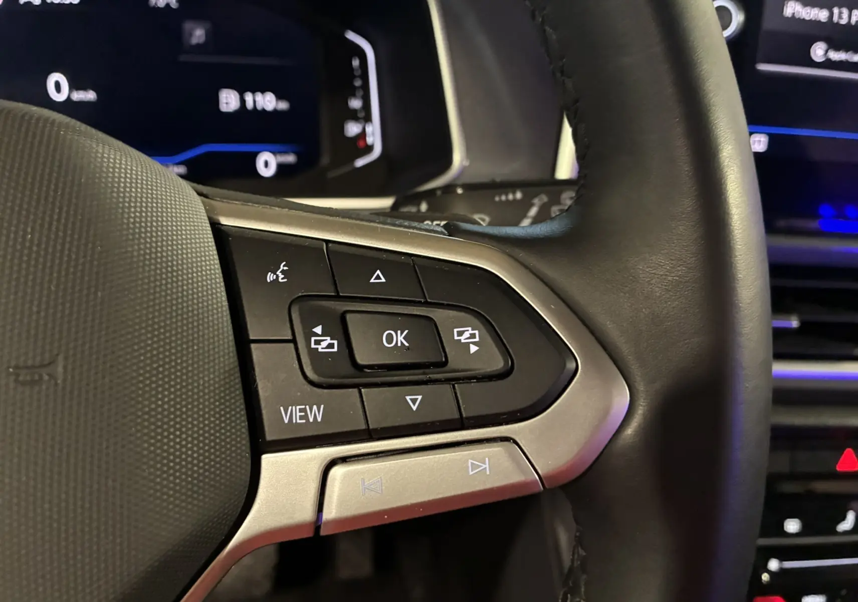 Gros plan sur les commandes multifonctions à gauche du volant noir du Volkswagen T-Roc gris, avec affichage numérique en arrière-plan.