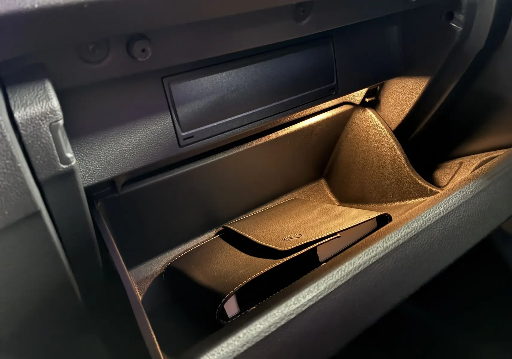 Vue rapprochée de la boîte à gants ouverte du Volkswagen T-Roc 2023, avec un étui en cuir noir à l'intérieur.