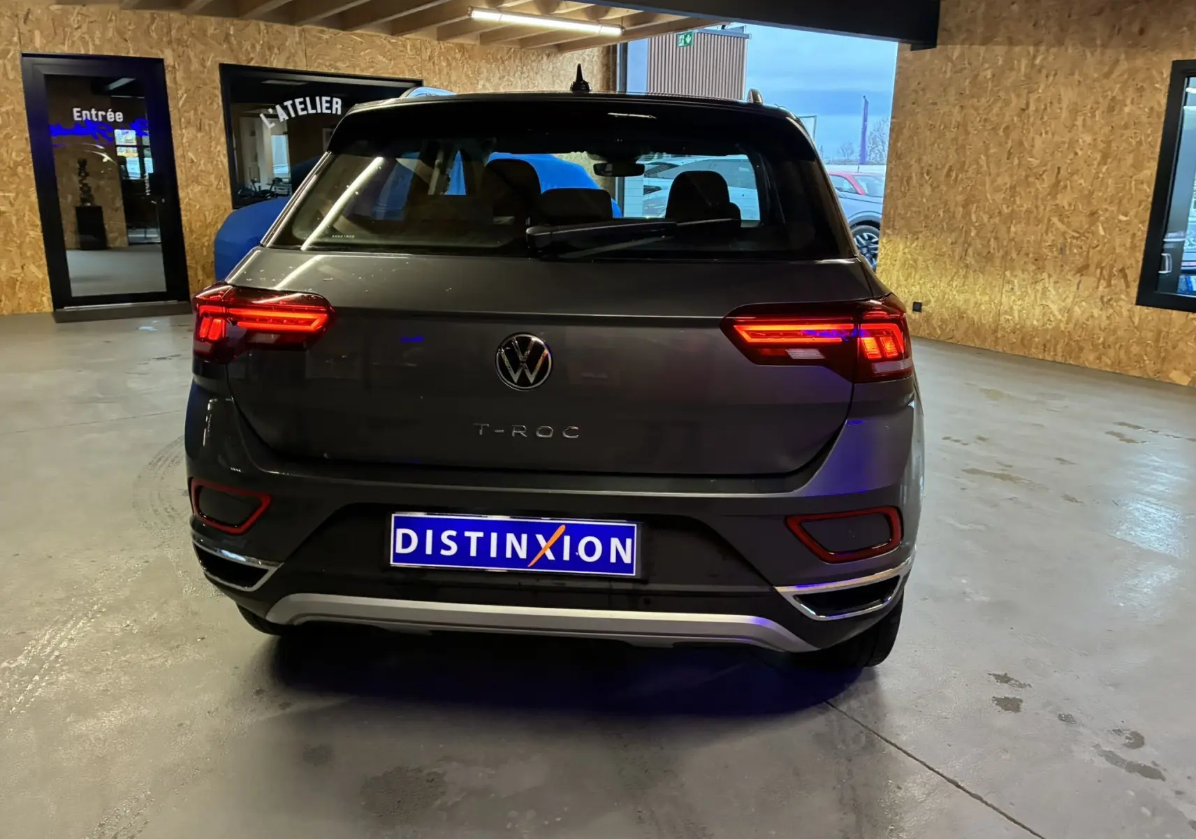 Vue arrière d'un Volkswagen T-Roc gris 2023 avec feux allumés, stationné dans un garage intérieur.