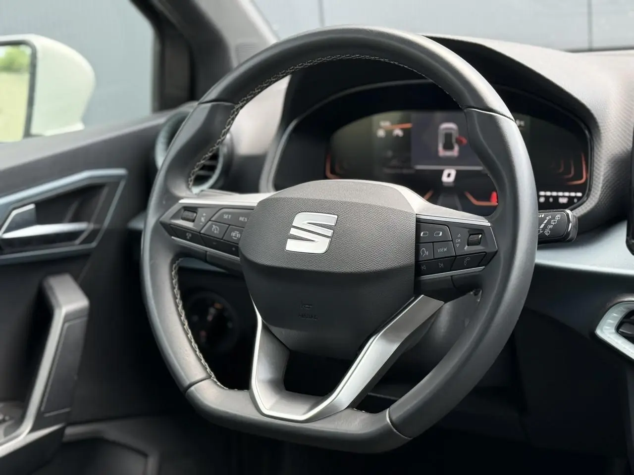 Vue rapprochée du volant noir du SEAT Arona 2025 avec commandes intégrées et tableau de bord digital en arrière-plan.