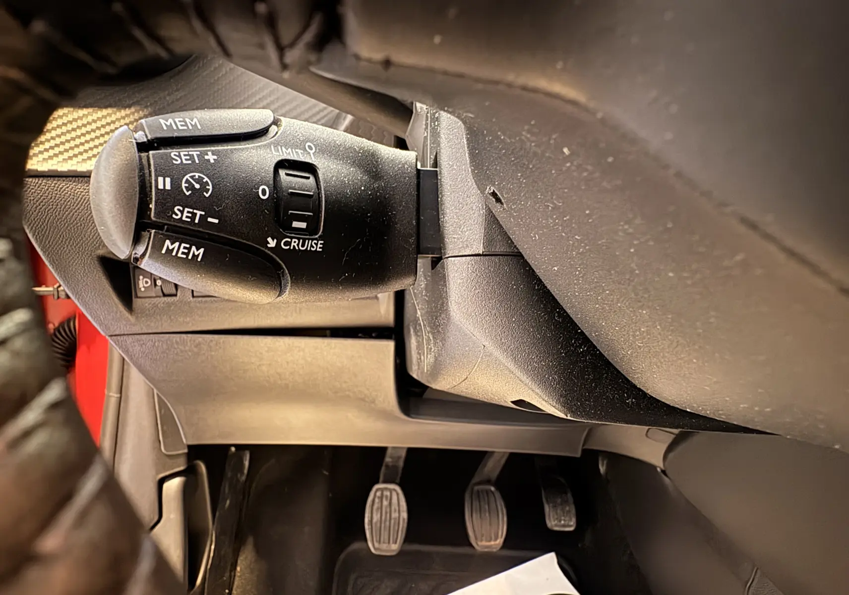 Gros plan sur la commande de régulateur de vitesse à gauche du volant dans l’habitacle d’une Peugeot 208 Active rouge 2024.