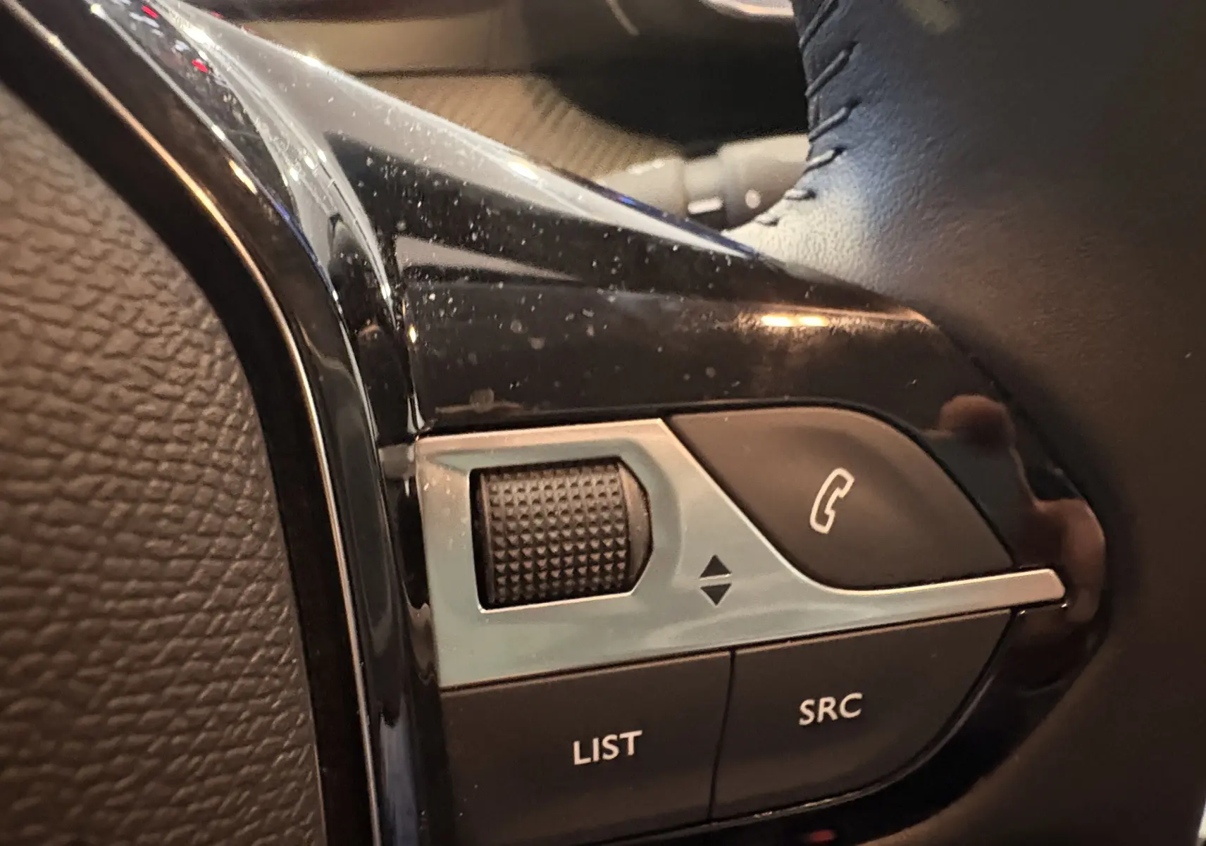 Gros plan sur les commandes au volant côté gauche de la Peugeot 208 Active rouge 2024, avec molette et boutons fonction audio.