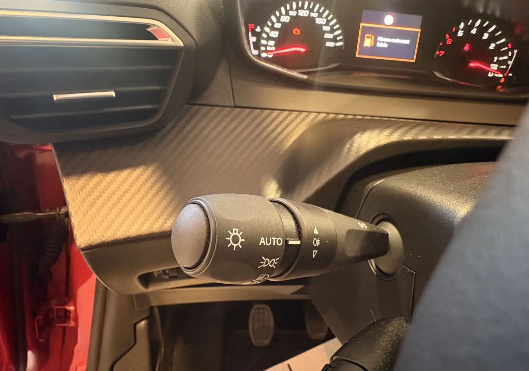 Détail du commodo d'éclairage avec tableau de bord allumé dans l'habitacle rouge d'une Peugeot 208 Active 2024.