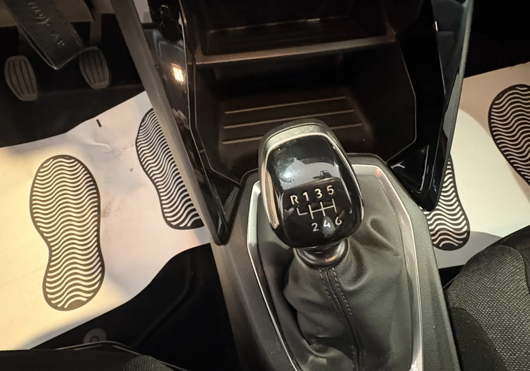 Gros plan sur le levier de vitesses manuel noir de la Peugeot 208 Active 2024, entouré de tapis blancs avec empreintes.