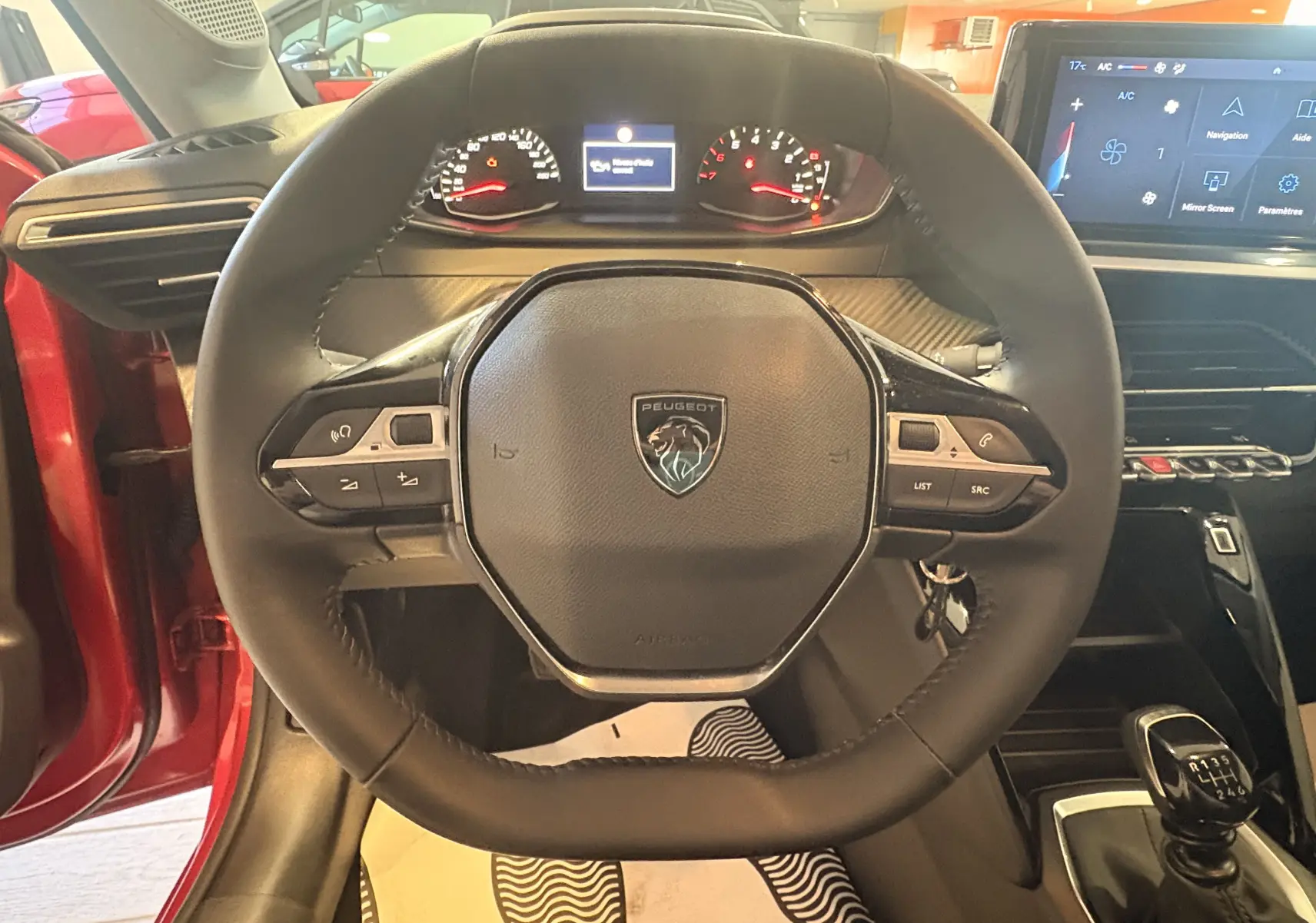 Vue centrée sur le volant et le tableau de bord d’une Peugeot 208 rouge 2024 avec boîte manuelle et écran tactile.