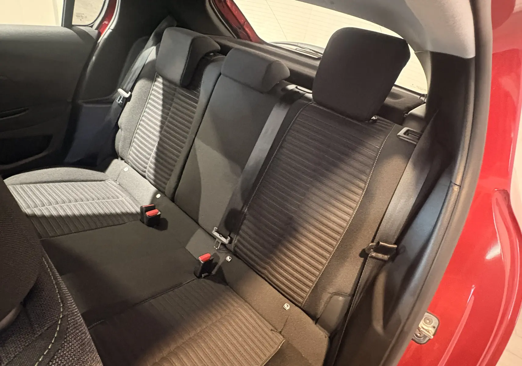 Vue intérieure arrière droite des sièges noirs en tissu de la Peugeot 208 Active rouge 2024 avec ceinture de sécurité visible.