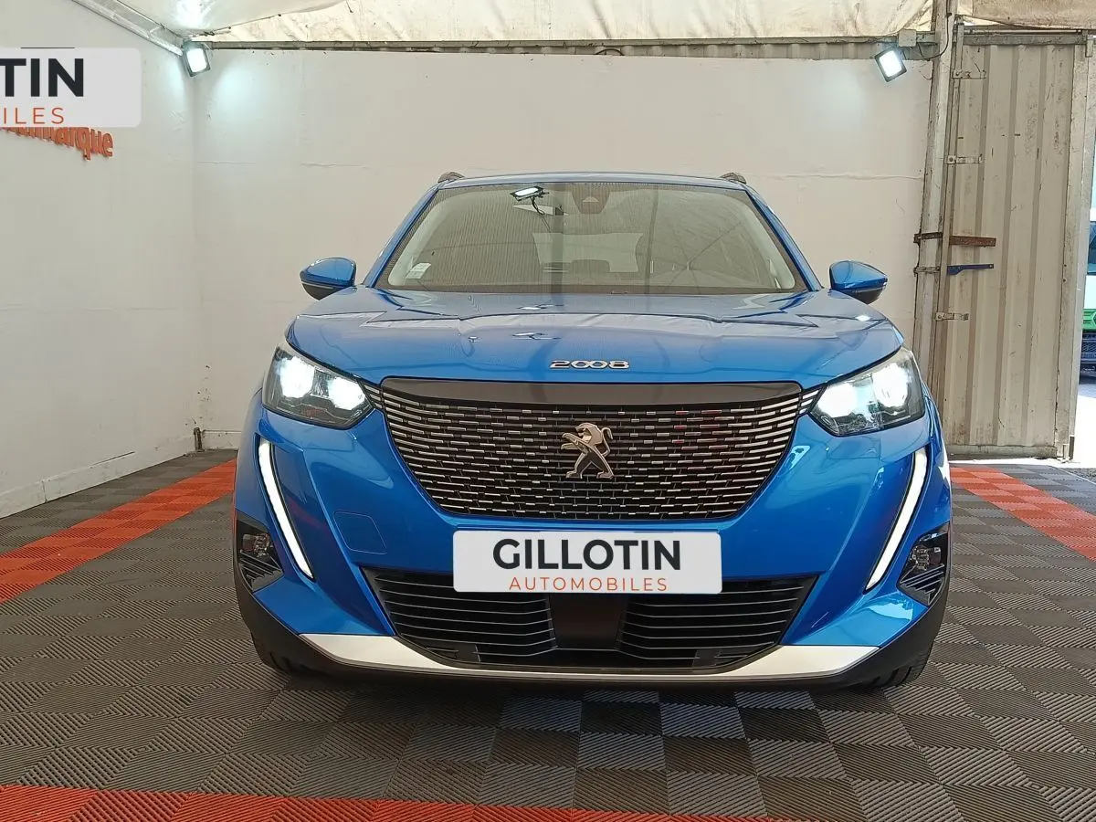 Vue frontale d'un Peugeot 2008 bleu avec calandre noire et feux LED allumés dans un showroom.