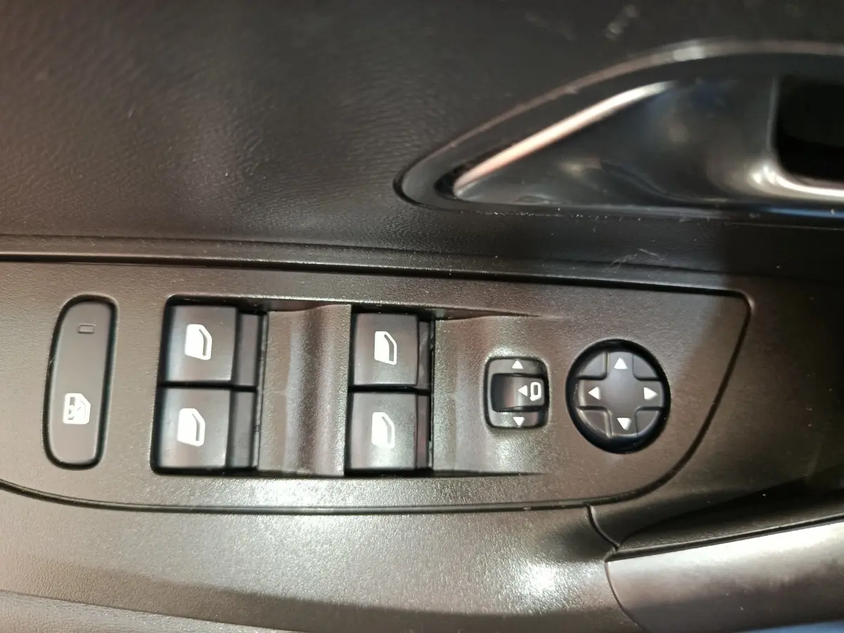 Gros plan sur les commandes de lève-vitres et réglage des rétroviseurs côté conducteur d'une Peugeot 2008 bleu 2021.