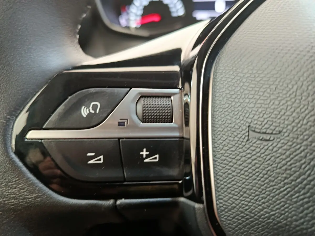 Gros plan sur les commandes multifonctions du volant cuir noir du Peugeot 2008 PureTech 100 S&S Allure Pack.