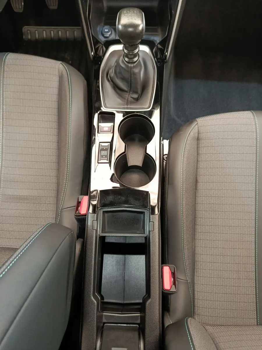 Vue plongeante sur la console centrale noire et la boîte manuelle entre les sièges gris à surpiqûres bleues du Peugeot 2008.