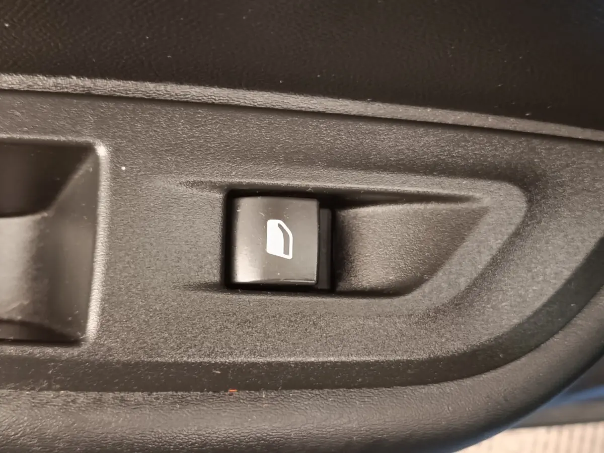 Bouton de commande de lève-vitre électrique noir sur panneau intérieur d'une Peugeot 2008 PureTech bleu, vue rapprochée.