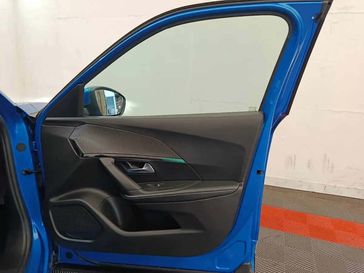 Vue intérieure de la porte avant gauche bleu vif d'une Peugeot 2008 avec garniture noire et insert décoratif texturé.